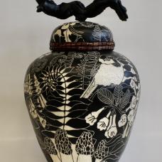 The lid of the jar is edged with woven pine needles and has a stained grapevine wood handle. The images on the surface of the pot were created using sgraffito and depict flowers  insects  birds  mushrooms and ferns.