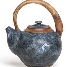 Teapot with crystalline glaze body and handle and base made to look like wood.