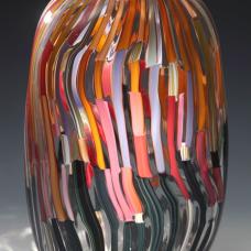 Blown glass form with multicolored cane work arranged in a rising dark to light pattern. This piece is shaped into a rounded rectangular form.