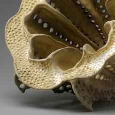 detail of an organic hollow porcelain form with grimy surface accenting the many circular indents covering the piece. 