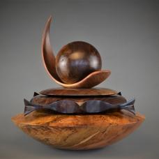 Black Walnut Burl Sphere (luna) rests upon the concave talon shaped Cherry swoosh and Black Walnut Disc. The ornate Black Walnut form features 2 kissing fish on each side and singing bird-heads on each corner which fits upon the large Spalted Maple hollowed out storage Vessel (base).